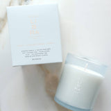 A white scented candle in a frosted glass jar next to its white packaging box, both featuring the brand name 'LIBRA' in a metallic rose-gold tone, set on a light marble surface.