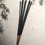 Black incense sticks on a light stone surface with greenery