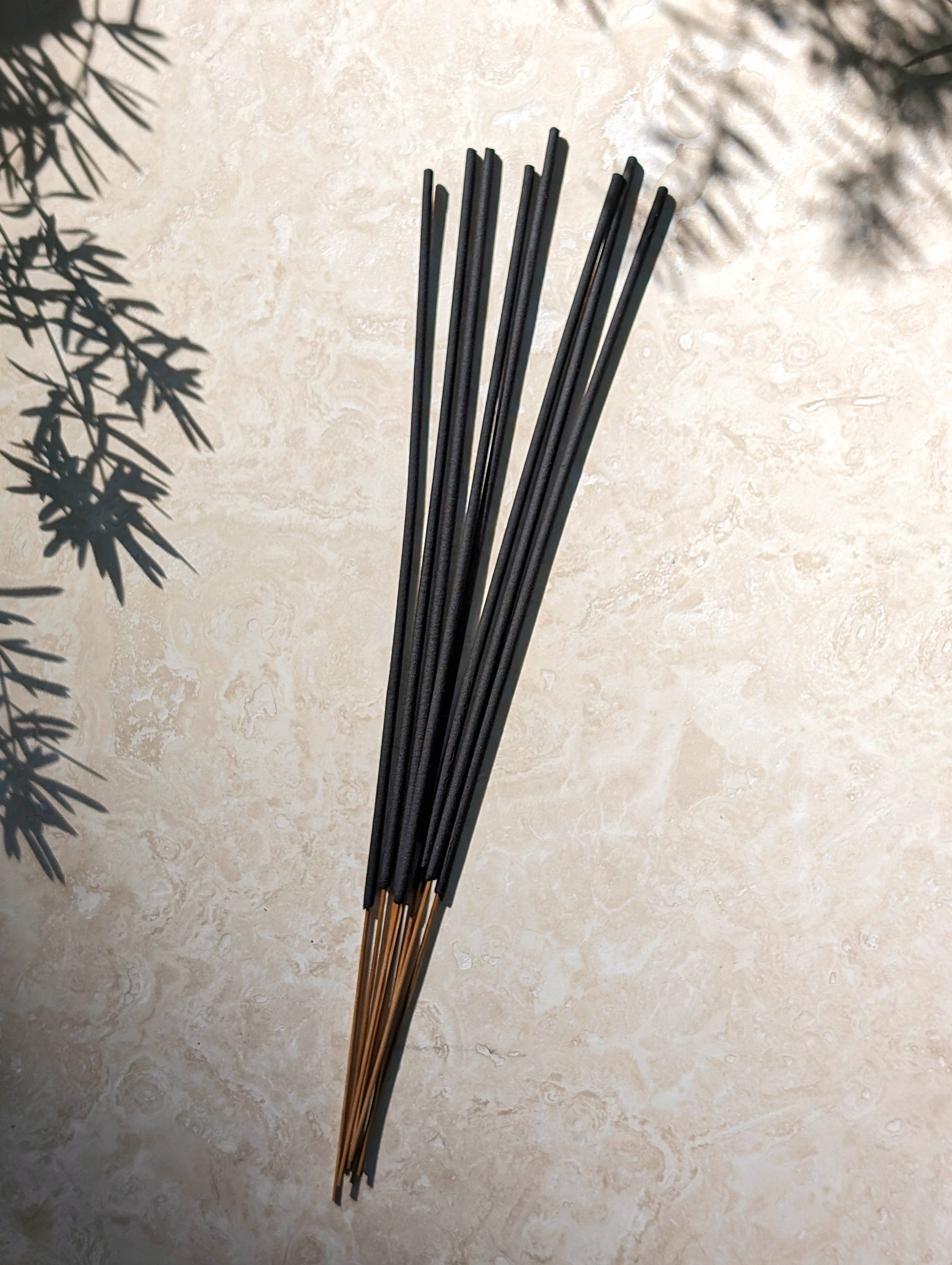 Black incense sticks on a light stone surface with greenery