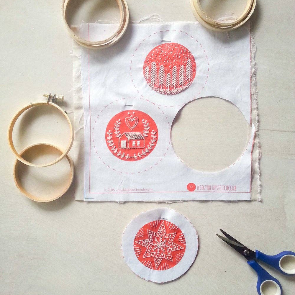 Embroidery hoops, fabric with red designs, and scissors on a light gray surface