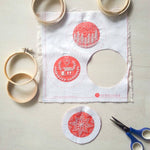 Embroidery hoops, fabric with red designs, and scissors on a light gray surface