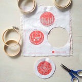 Embroidery hoops, fabric with red designs, and scissors on a light gray surface