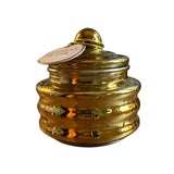 A small metallic gold lidded jar with a ribbed body and a hanging paper tag, photographed on a plain white background.