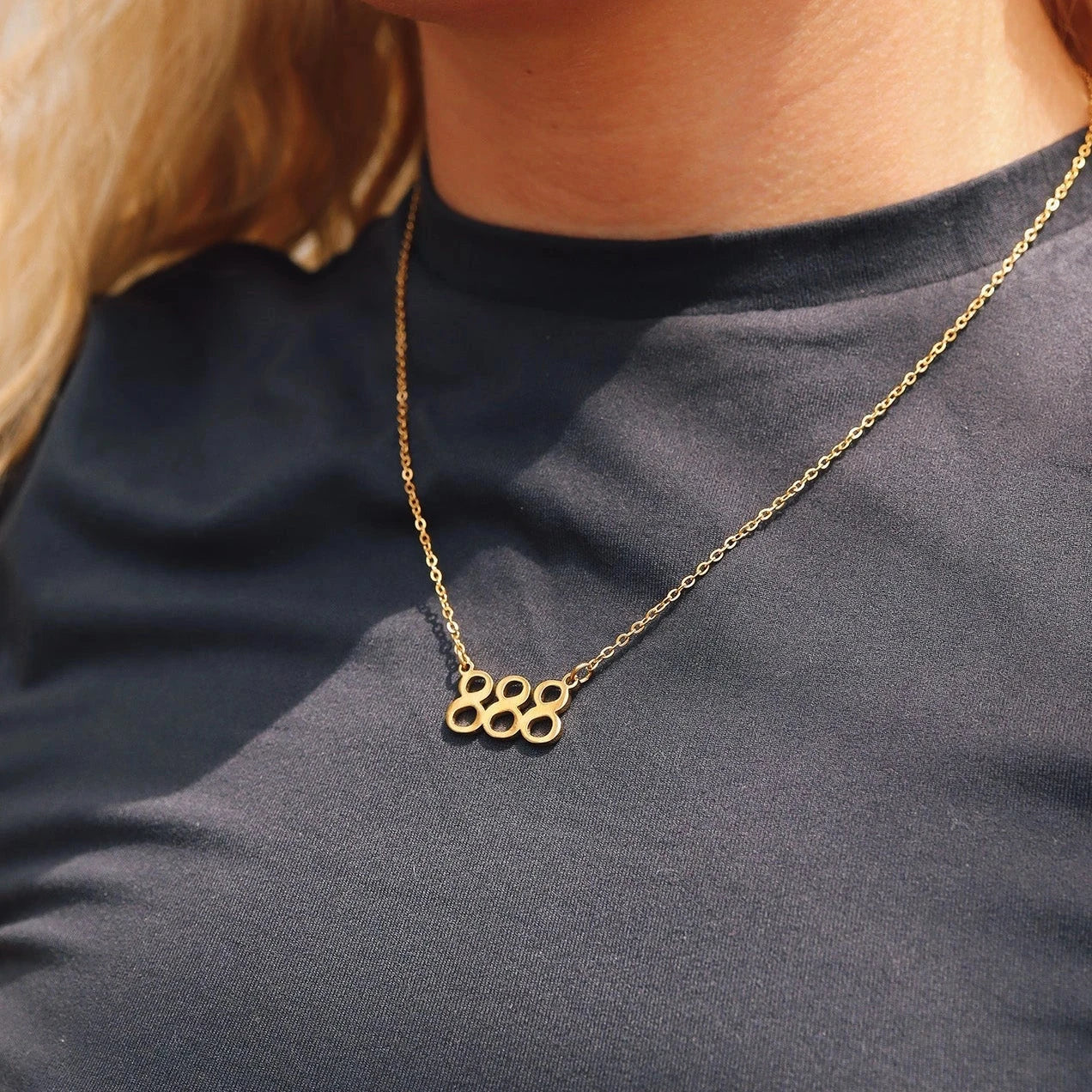 Gold necklace with '888' pendant on a person wearing a black shirt.