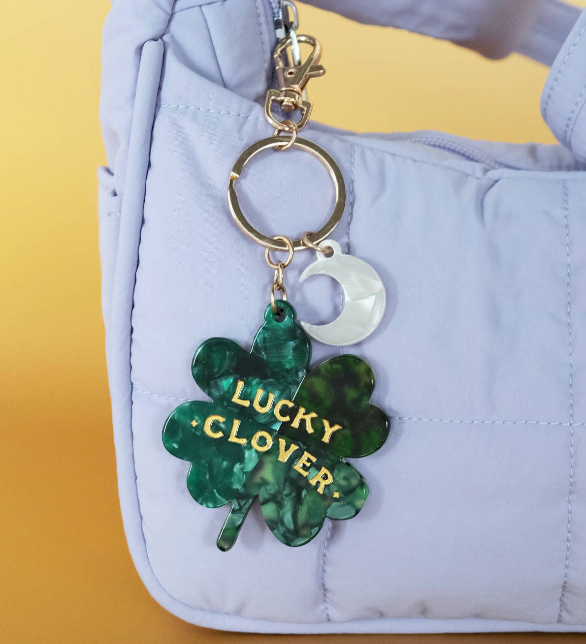 Green 'Lucky Clover' keychain on a light blue bag with a yellow background