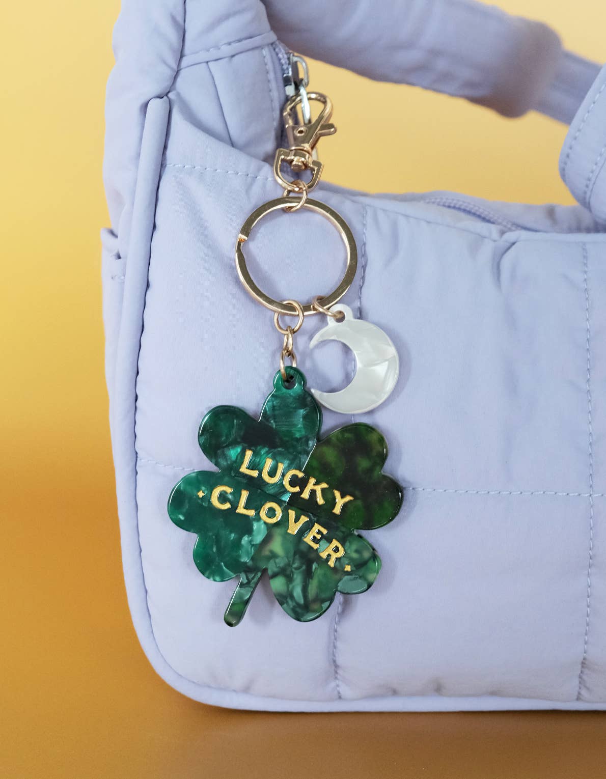 Green 'Lucky Clover' keychain on a light blue bag with a yellow background