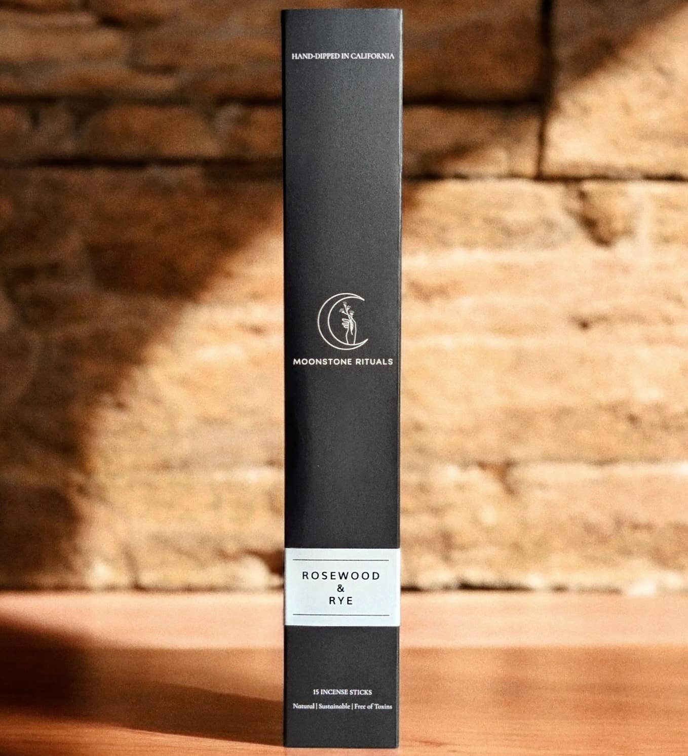Black cylindrical product box with branding on a wooden surface and brick wall background