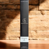 Black cylindrical product box with branding on a wooden surface and brick wall background