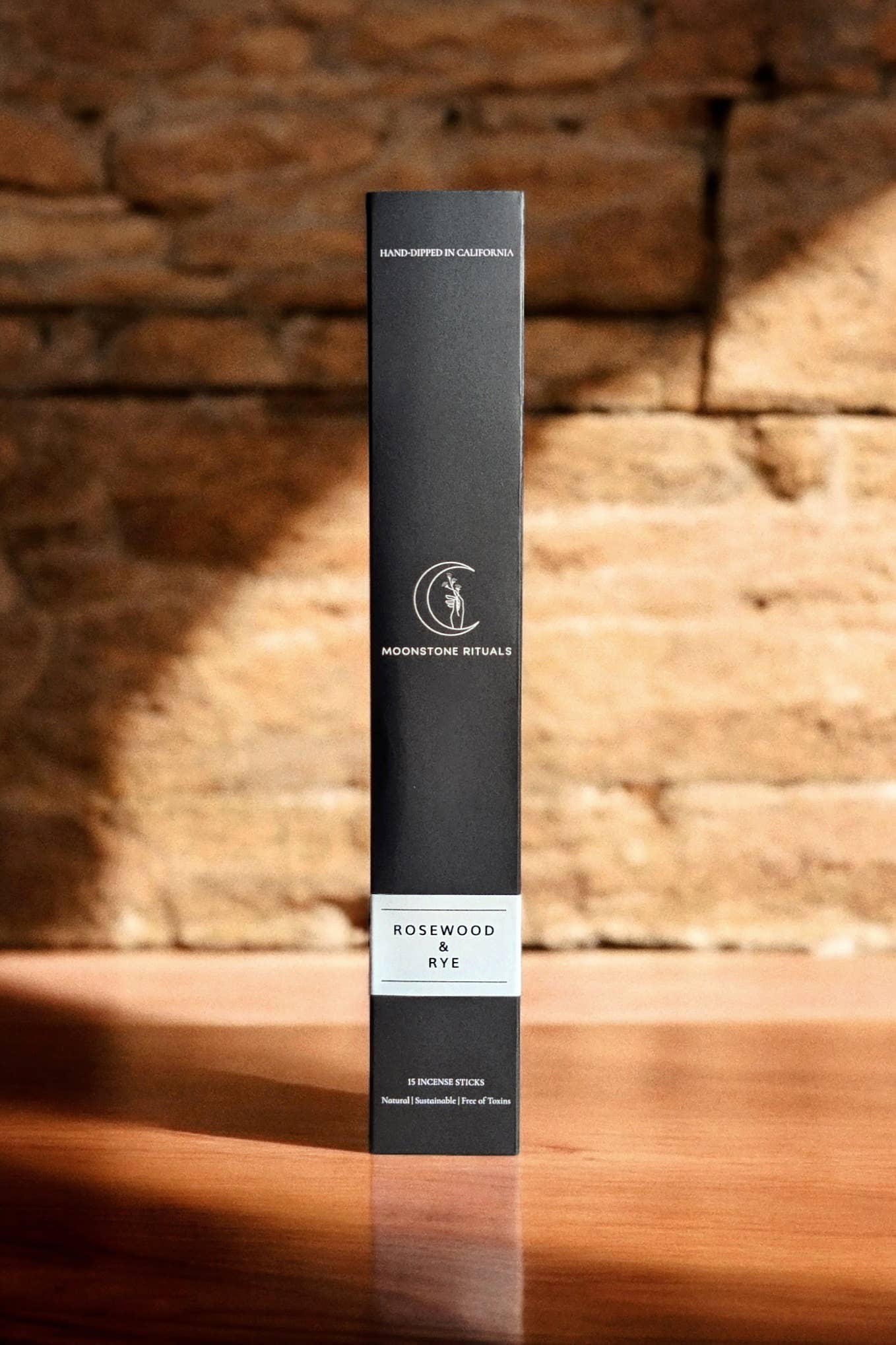 Black cylindrical product box with branding on a wooden surface and brick wall background