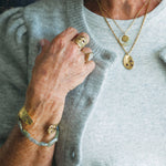 Close-up of a person wearing gold jewelry including rings and bracelets on a neutral background