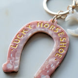 Pink horseshoe keychain with 'Lucky Horseshoe' text on a light background