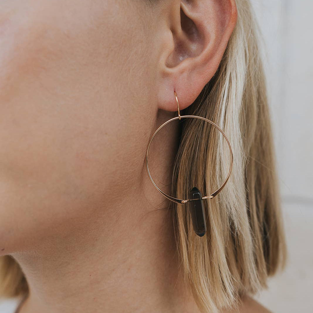 Close-up of a person wearing gold hoop earrings with a neutral background