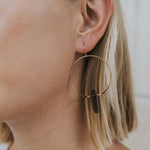 Close-up of a person wearing gold hoop earrings with a neutral background