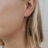Close-up of a person wearing gold hoop earrings with a neutral background