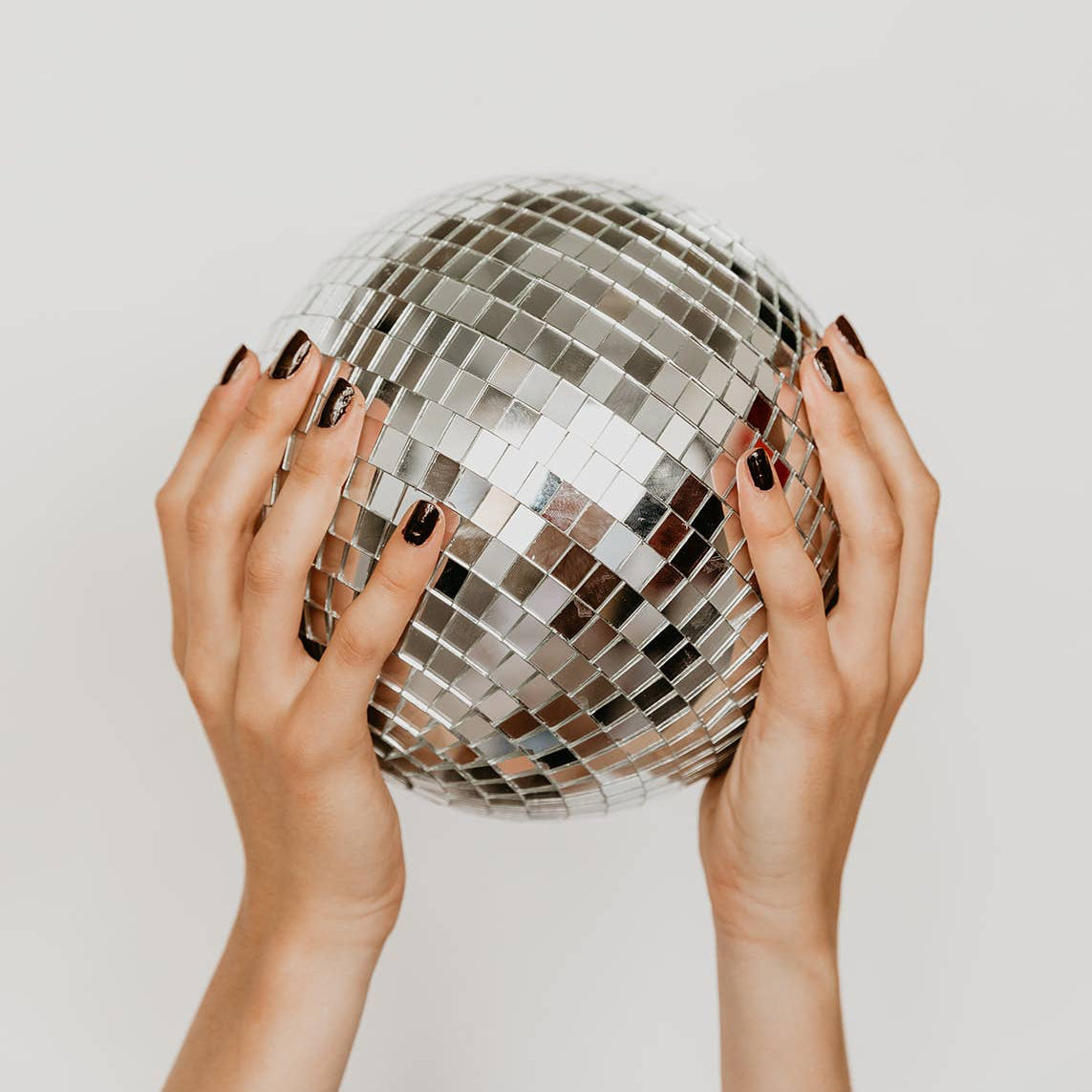 Hands holding a disco ball against a plain background