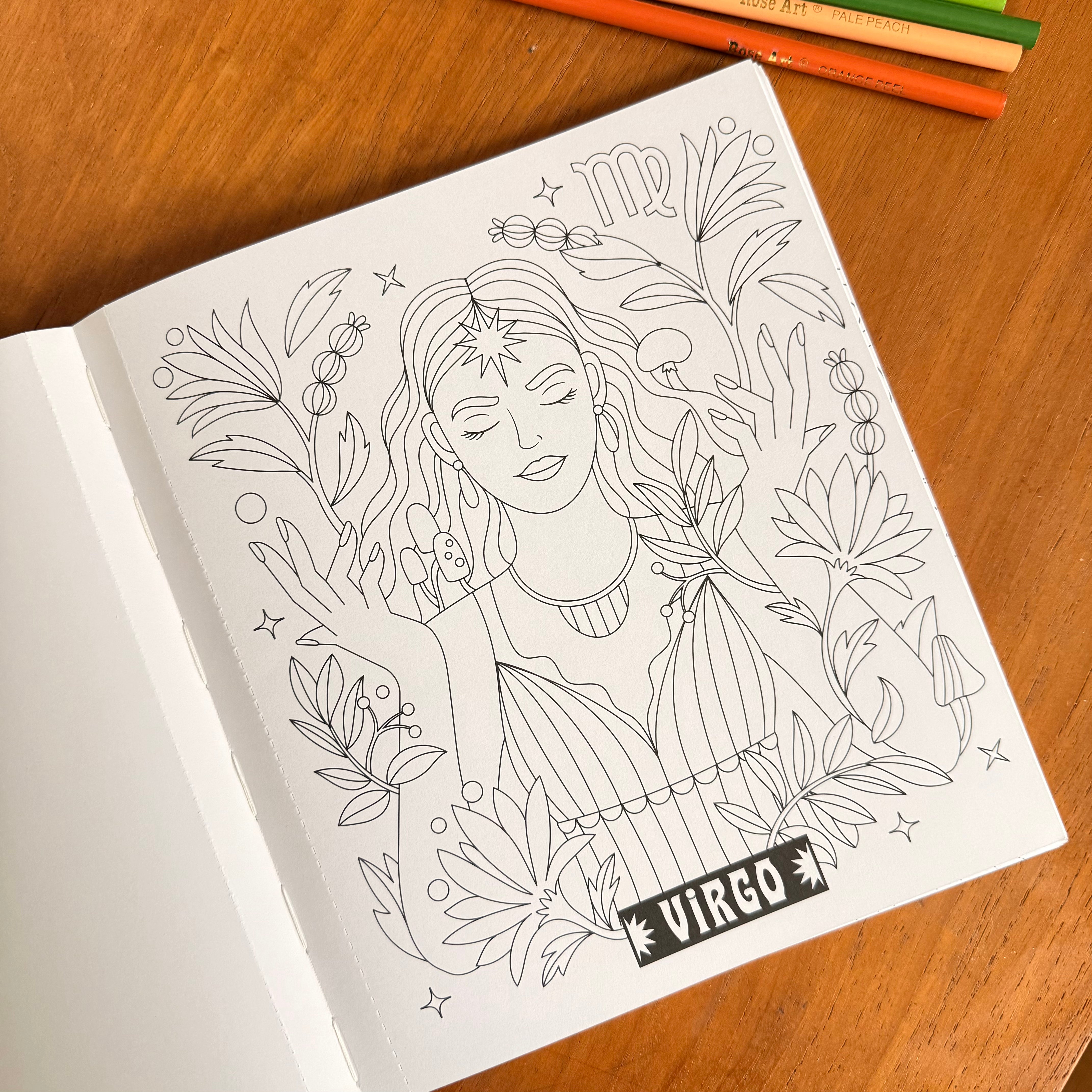 A black and white line art coloring page featuring a Virgo woman surrounded by plants, shown on a wooden table with colored pencils in the background.