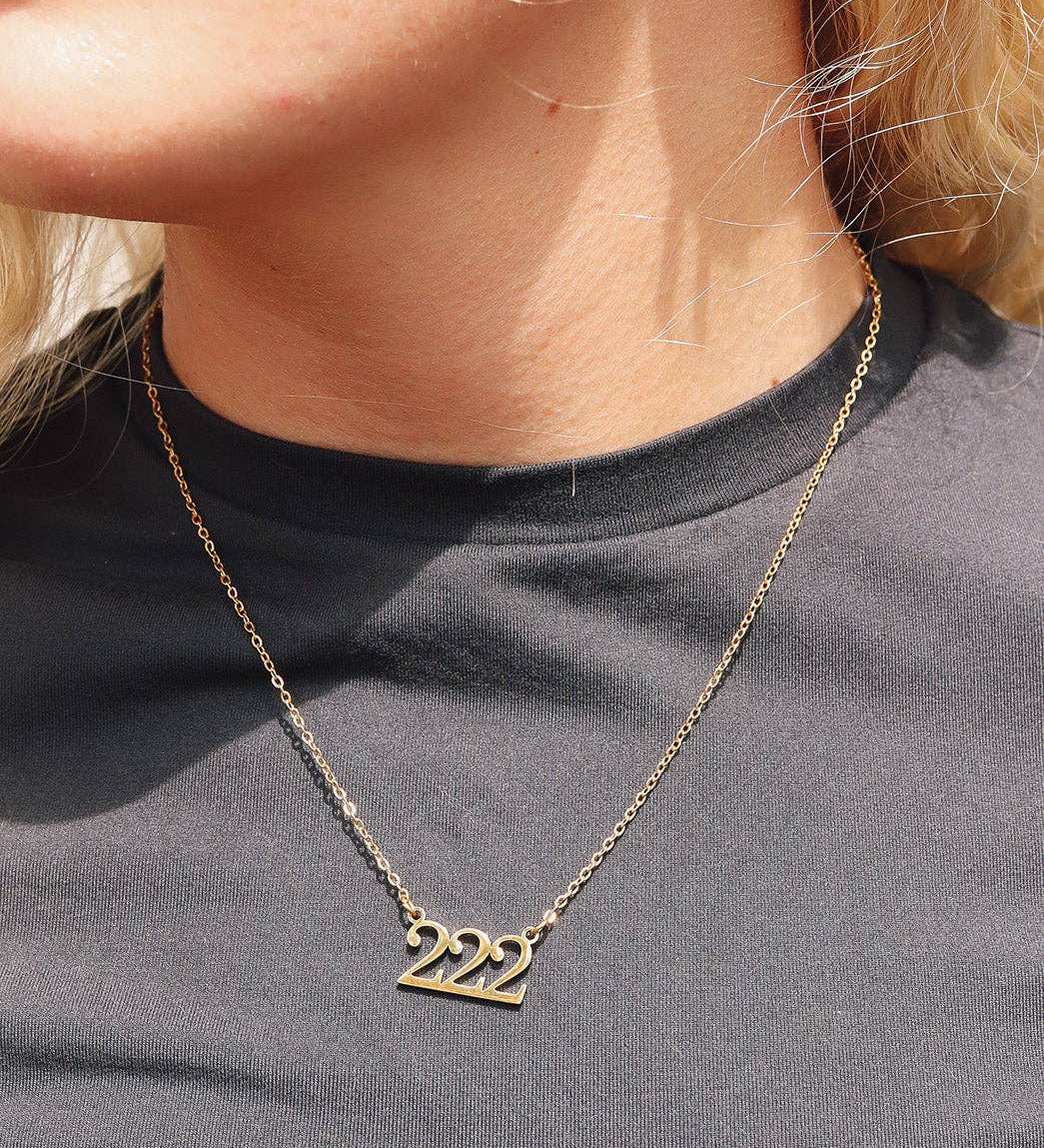 Gold necklace with '222' pendant worn by a person on a plain background