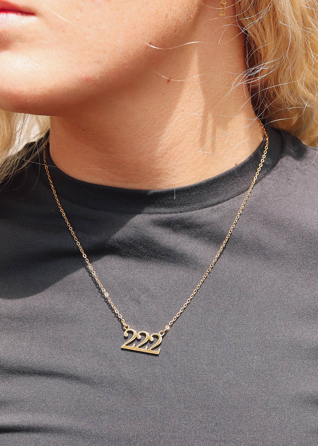Gold necklace with '222' pendant worn by a person on a plain background