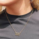 Gold necklace with '222' pendant worn by a person on a plain background