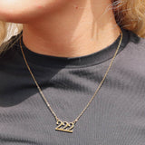 Gold necklace with '222' pendant worn by a person on a plain background