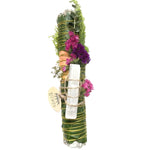 Decorative bundle with greenery, flowers, and a white candle on a white background