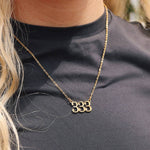 Gold necklace with a unique design worn by a person against a black background