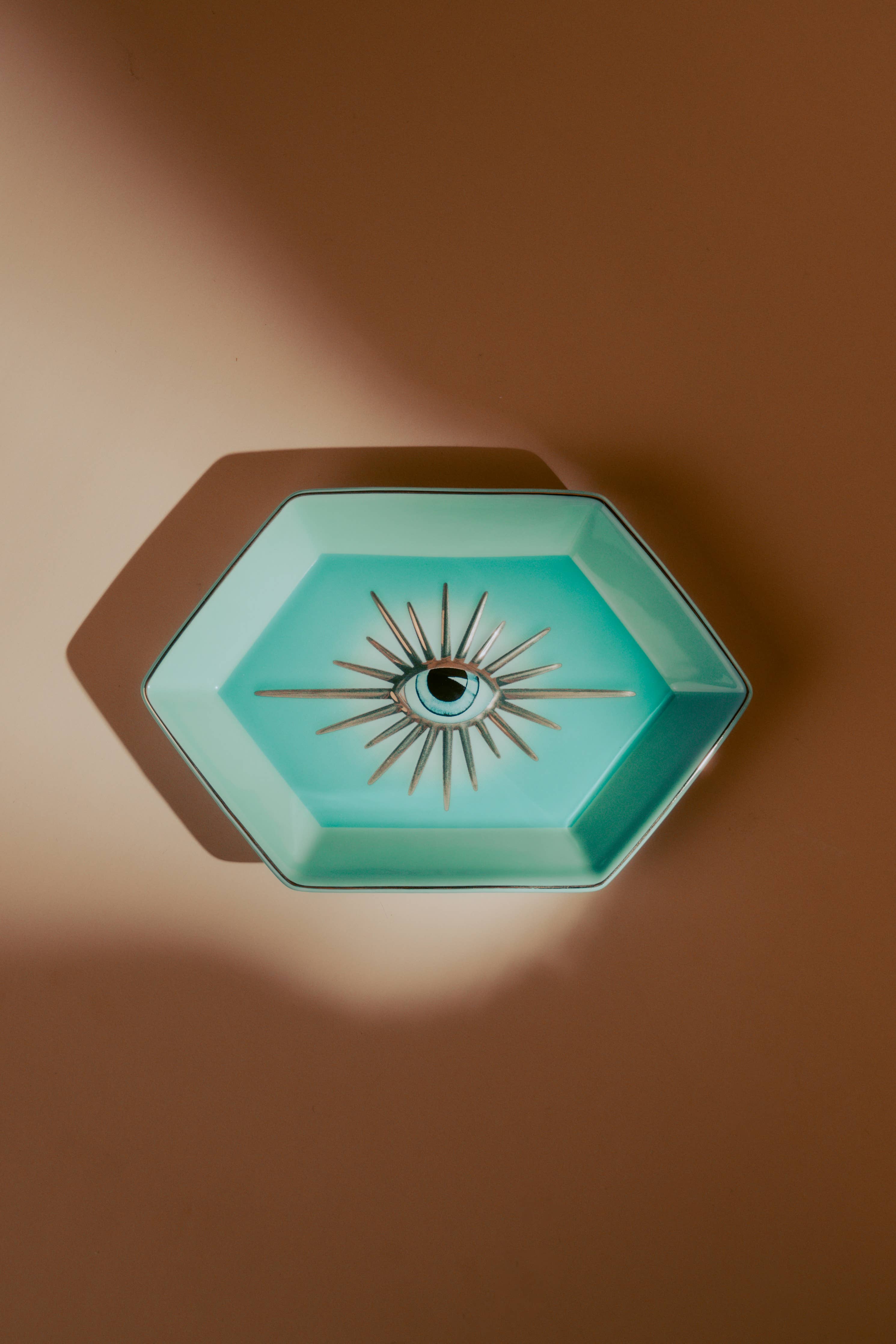 Hexagonal turquoise dish with eye design on a brown background