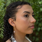Woman with braided hair wearing earrings against a green leafy background