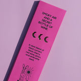 Bright pink rectangular product packaging for Brass Earth wine, photographed at an angle on a matching pink background. The box features black text reading 'SMOKY AIR AND A SECRET BOTTLE OF WINE.