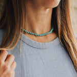 Close-up of a person wearing a turquoise beaded necklace with a blurred background