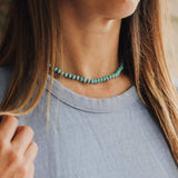 Close-up of a person wearing a turquoise beaded necklace with a blurred background