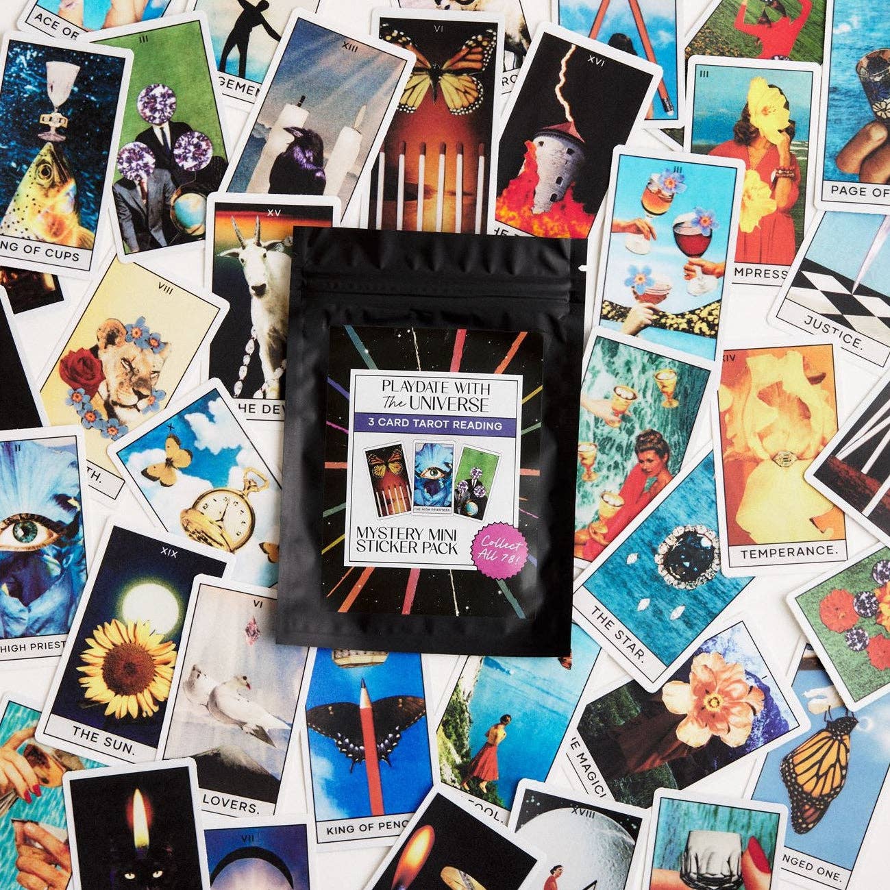 A black resealable pouch labeled 'Playdate with the Universe Mystery Mini Sticker Pack' sits on top of a scattered arrangement of colorful tarot cards.