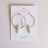 Gold hoop earrings with green stones on a Jaxtelly branded card.