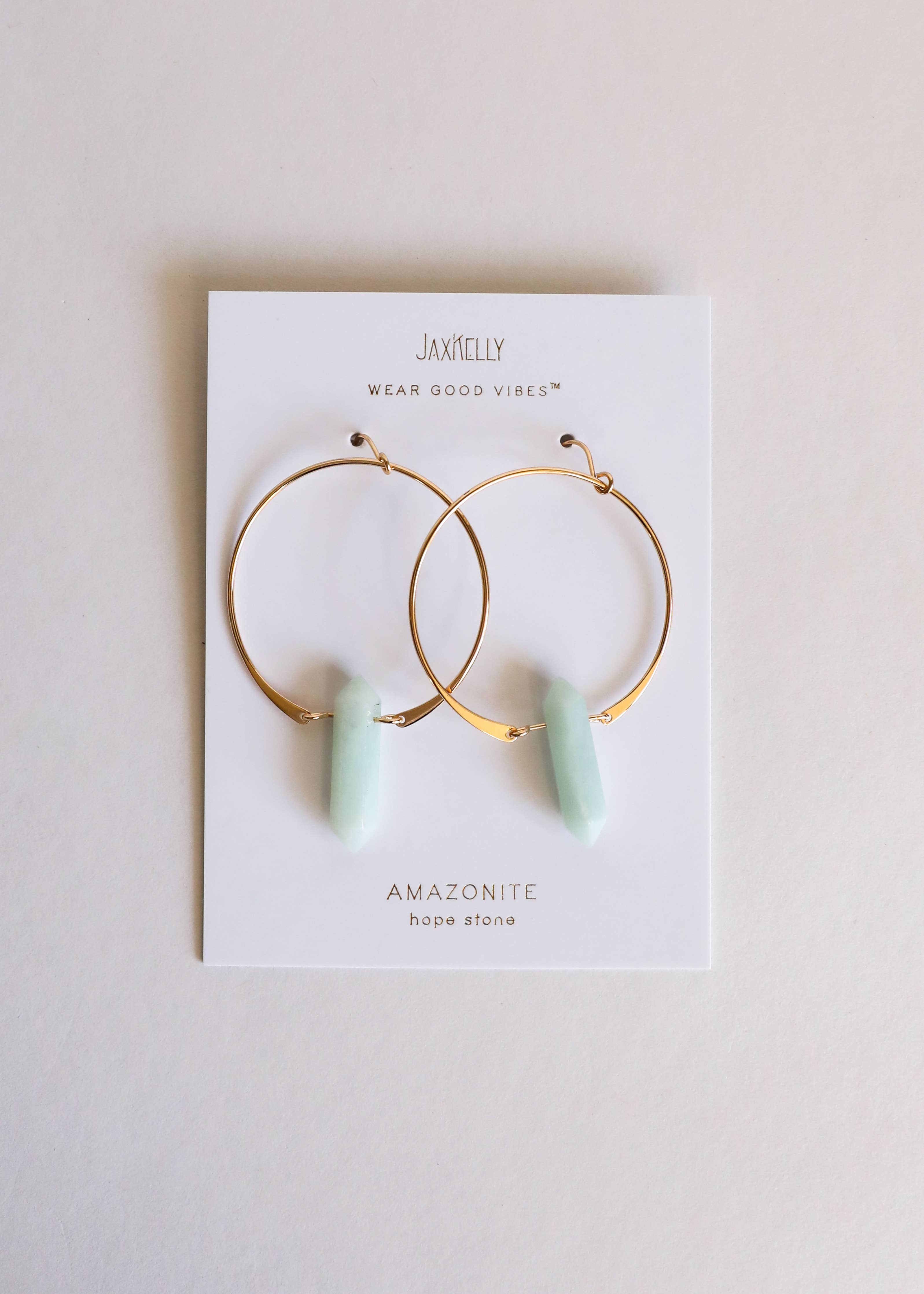 Gold hoop earrings with green stones on a Jaxtelly branded card.