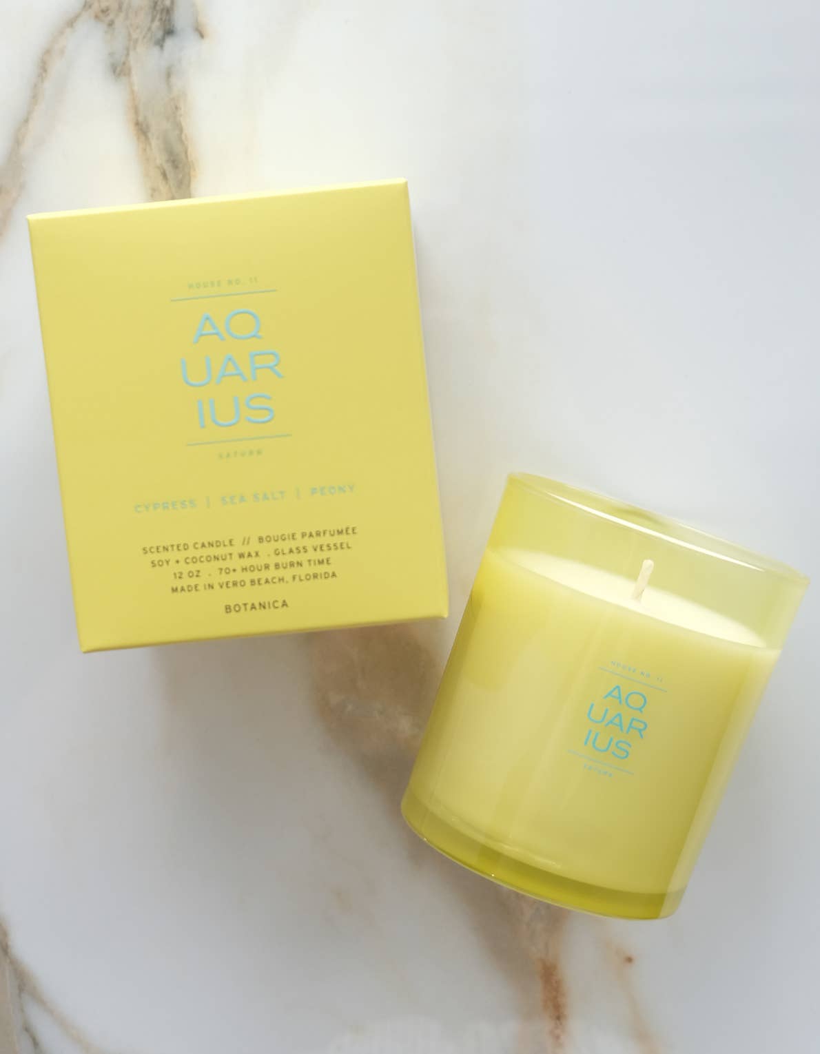 Yellow candle and packaging labeled 'Aquarius' on a marble surface