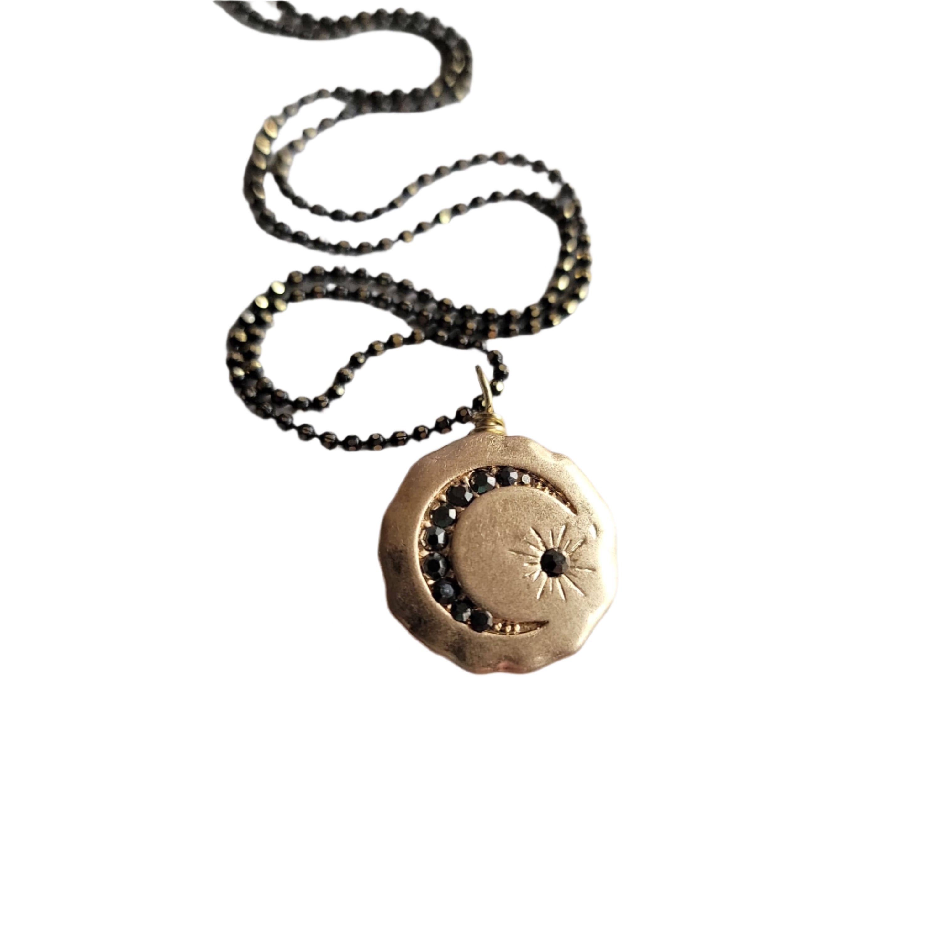 Gold necklace with a circular pendant and moon on a textured surface