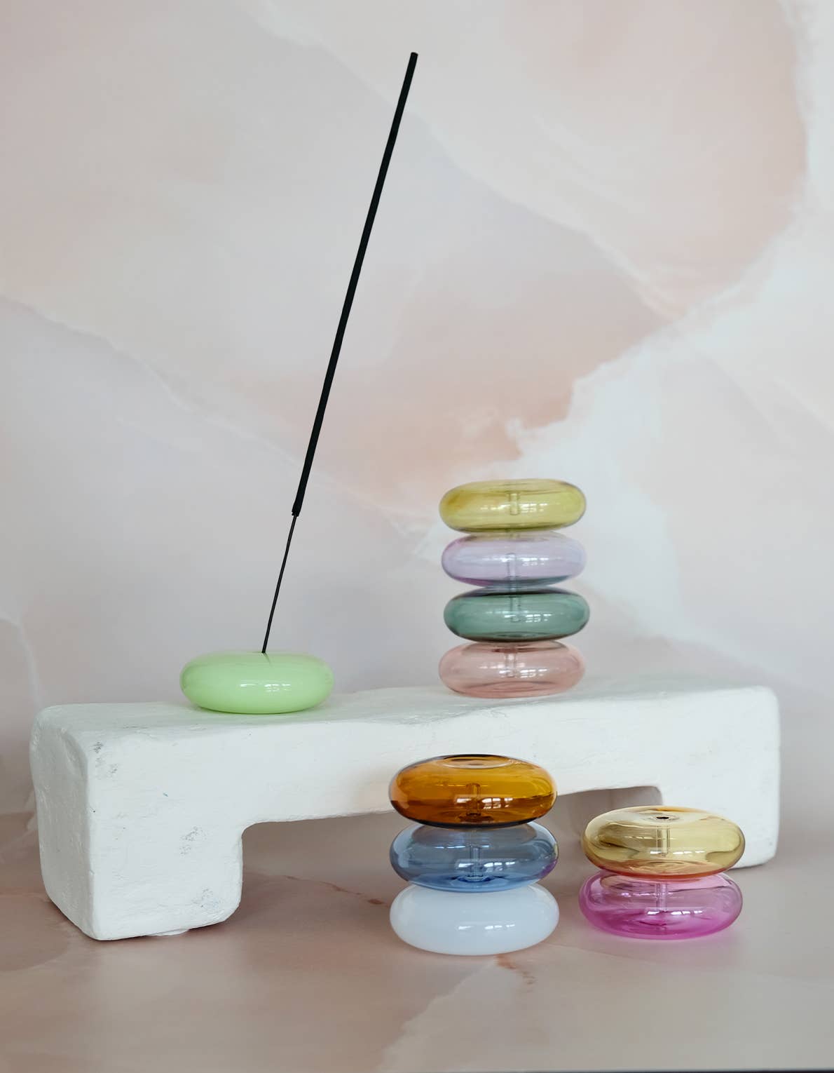 Stacks of colorful rings on a white block with a black incense stick against a light background