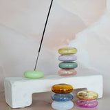 Stacks of colorful rings on a white block with a black incense stick against a light background