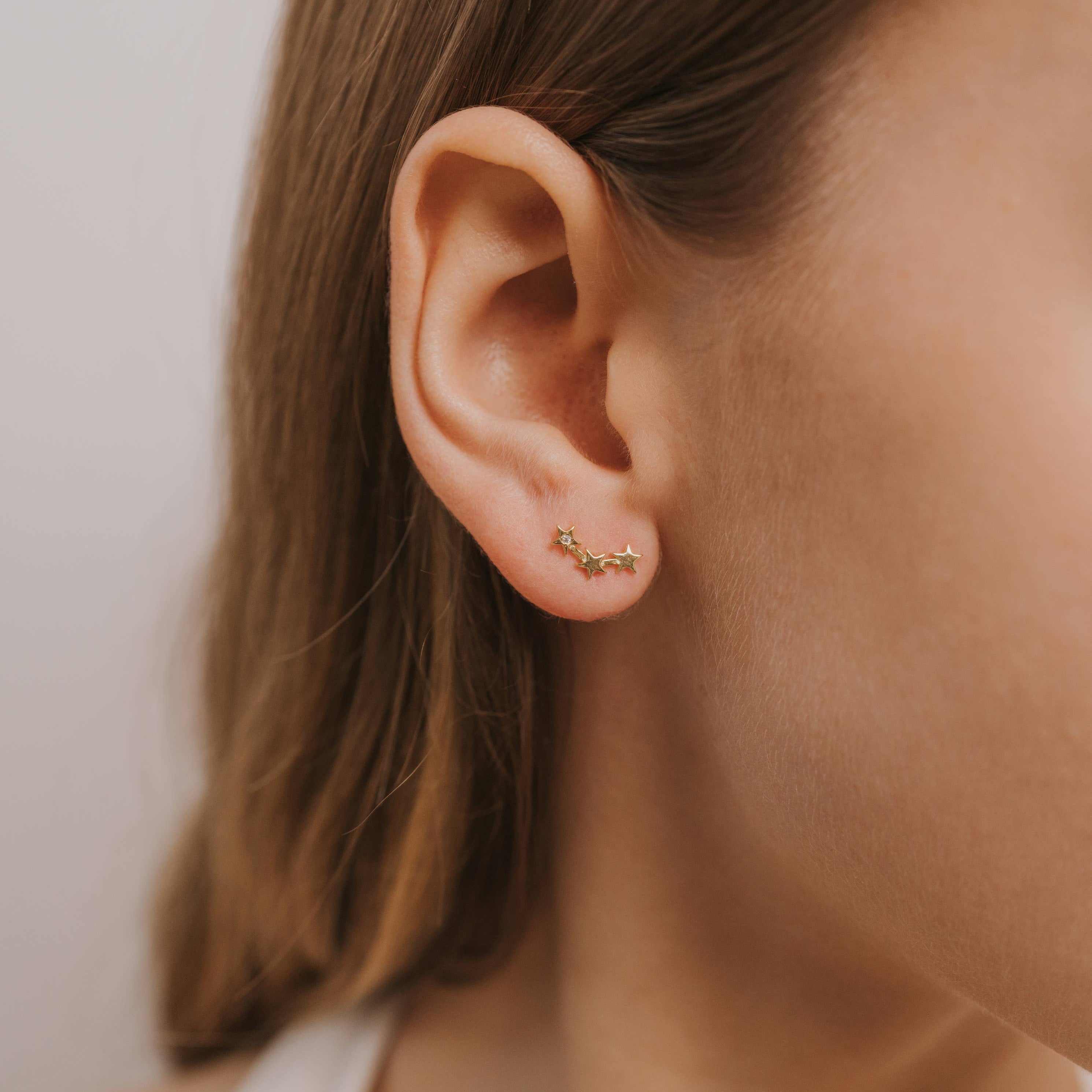 Close-up of an ear wearing a small gold earring with a neutral background