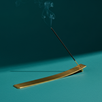Gold incense burner with a single incense stick on a teal background