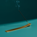 Gold incense burner with a single incense stick on a teal background