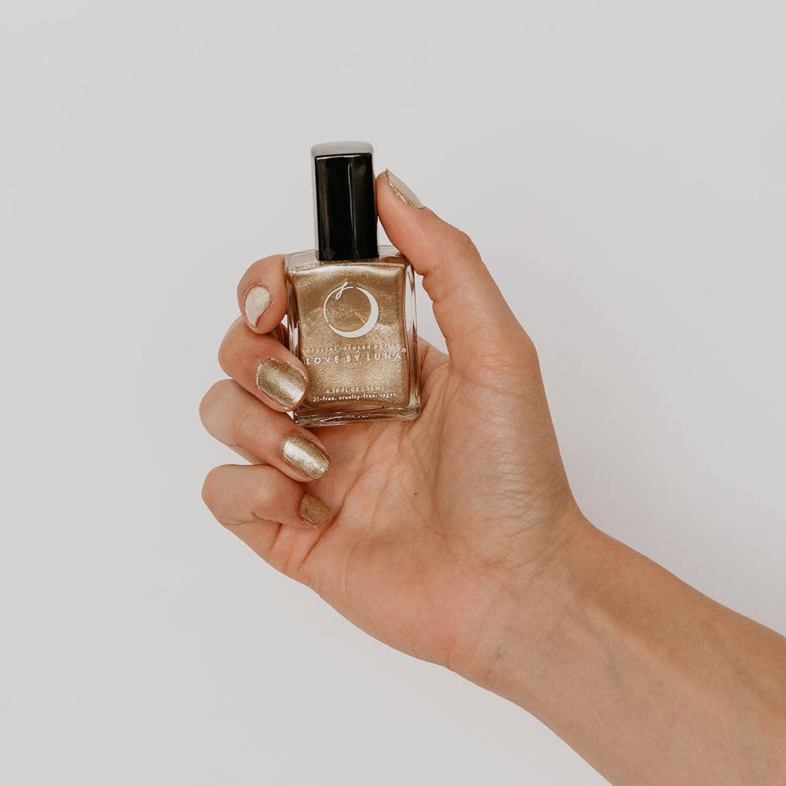 Hand holding a small bottle of nail polish against a plain background