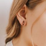 Close-up of a woman's ear wearing a gold earring with a plain background