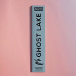 A tall, narrow light blue box for Brass Earth Ghost Lake incense sticks, standing vertically against a soft pink gradient background.
