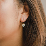 Close-up of an ear wearing a gold earring with a heart-shaped gemstone.