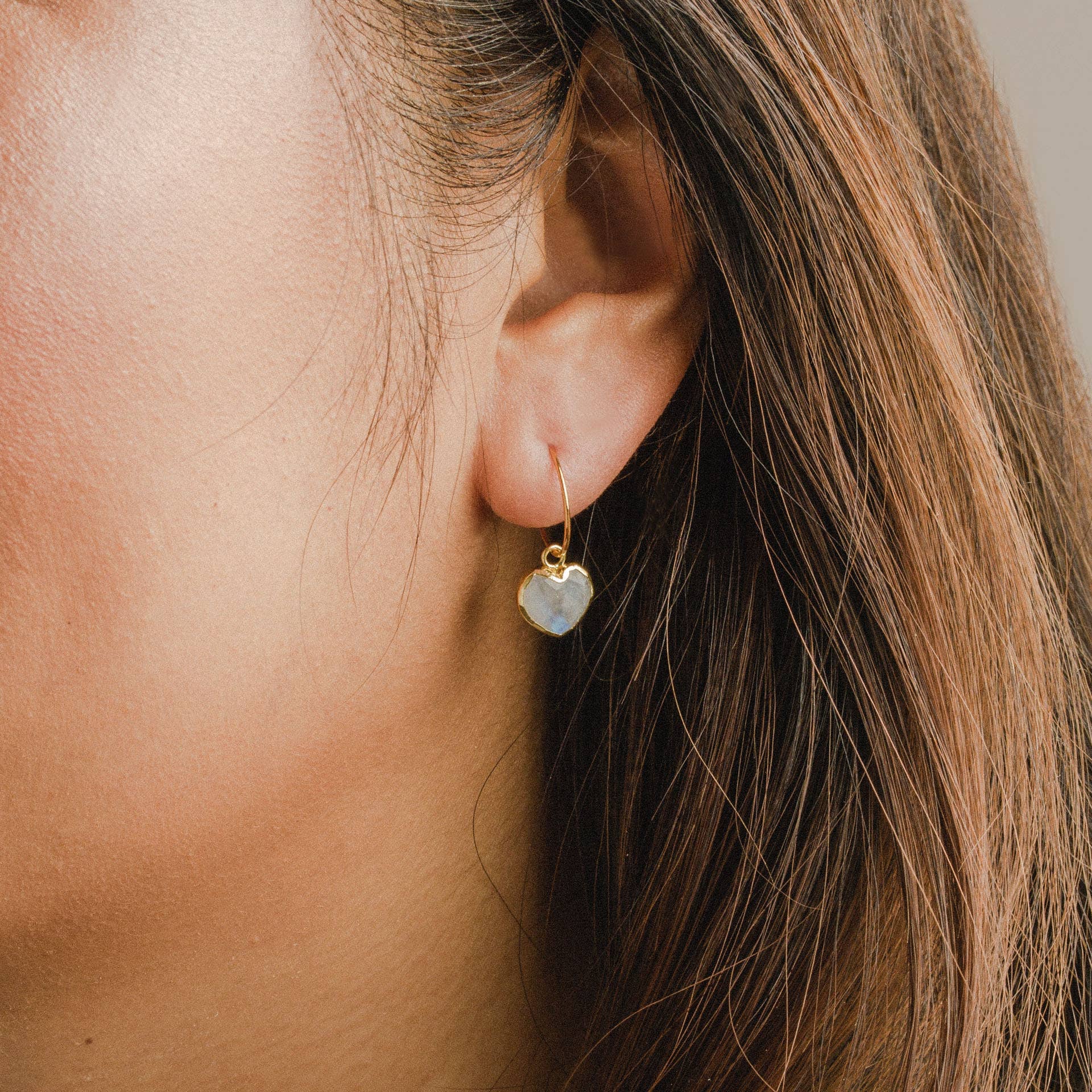 Close-up of an ear wearing a gold earring with a heart-shaped gemstone.