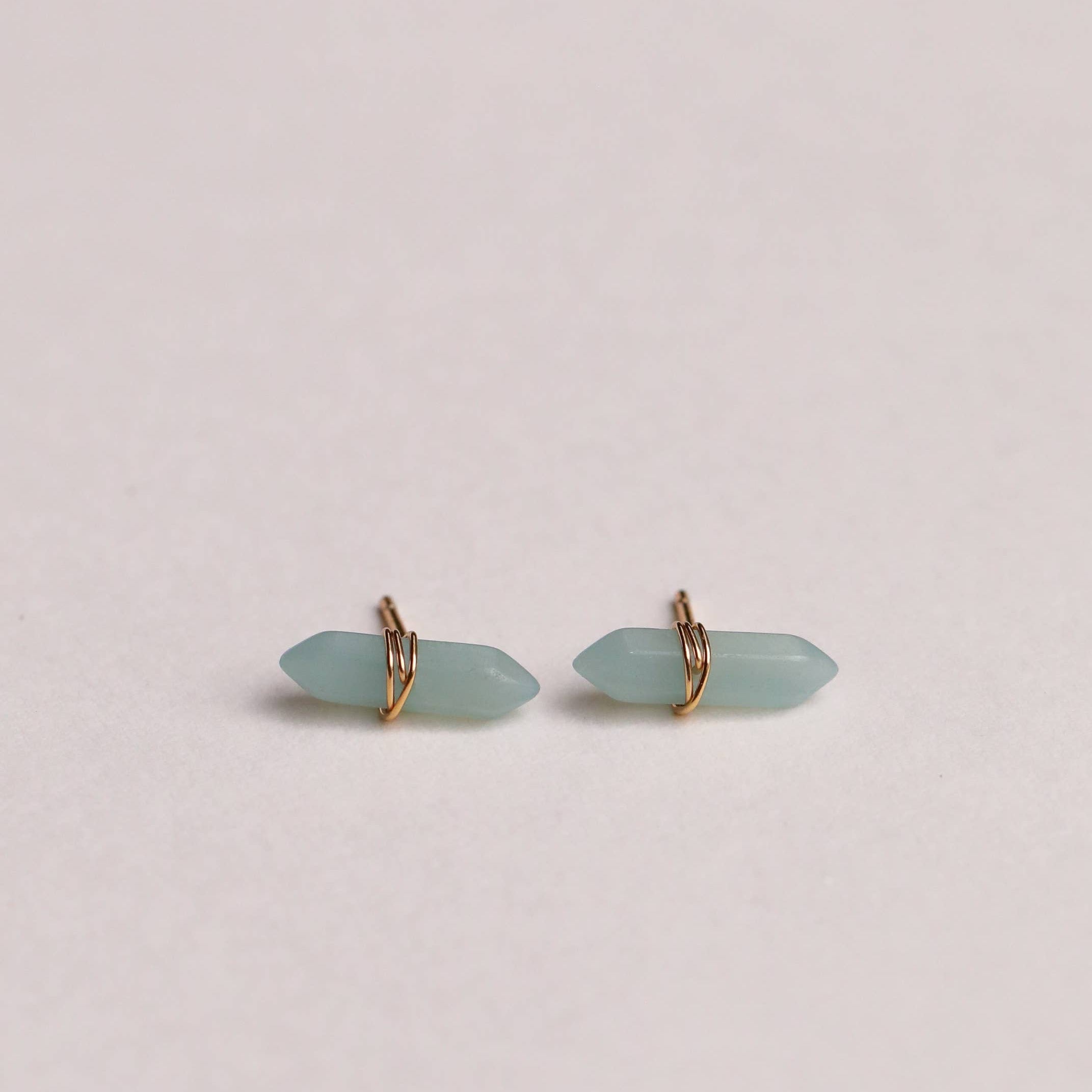 Pair of light blue earrings with gold accents on a beige background