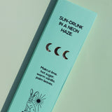 A mint green rectangular product box for Brass Earth, photographed at an angle on a matching mint background. The box features black text reading 'SUN-DRUNK IN A NEON HAZE.