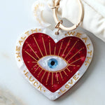 Heart-shaped keychain charm with eye design and text on a white surface