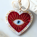 Heart-shaped keychain charm with eye design and text on a white surface